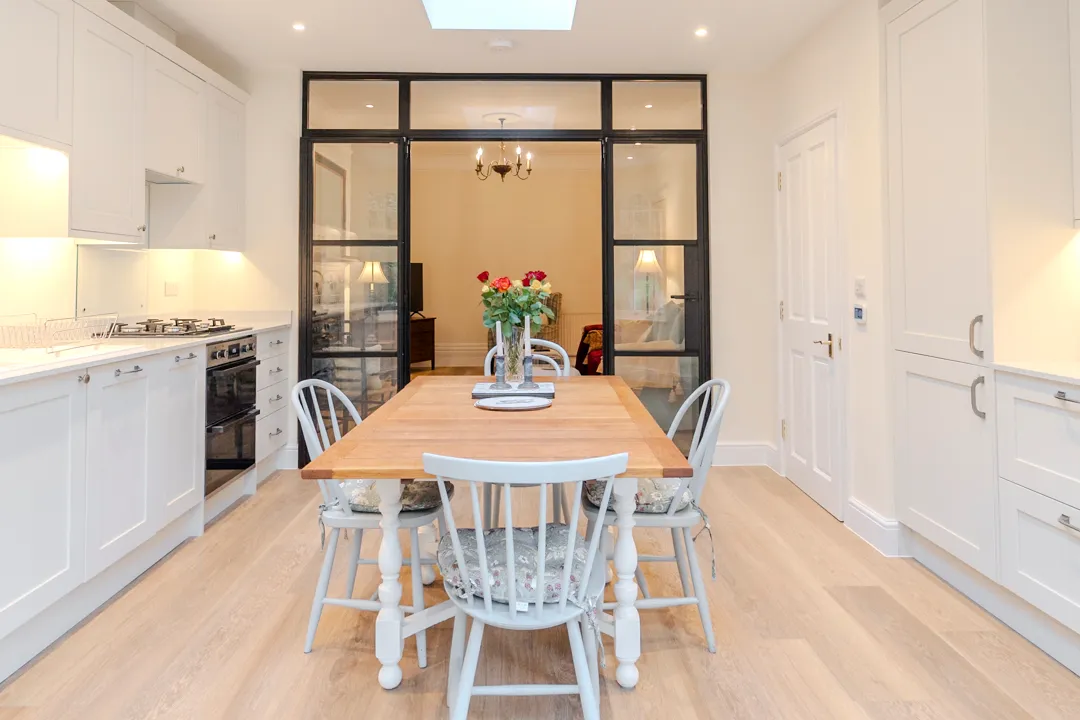 A kitchen with a wooden table surrounded by white chairs.